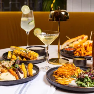 Cocktail on a table with lime garnish and food.