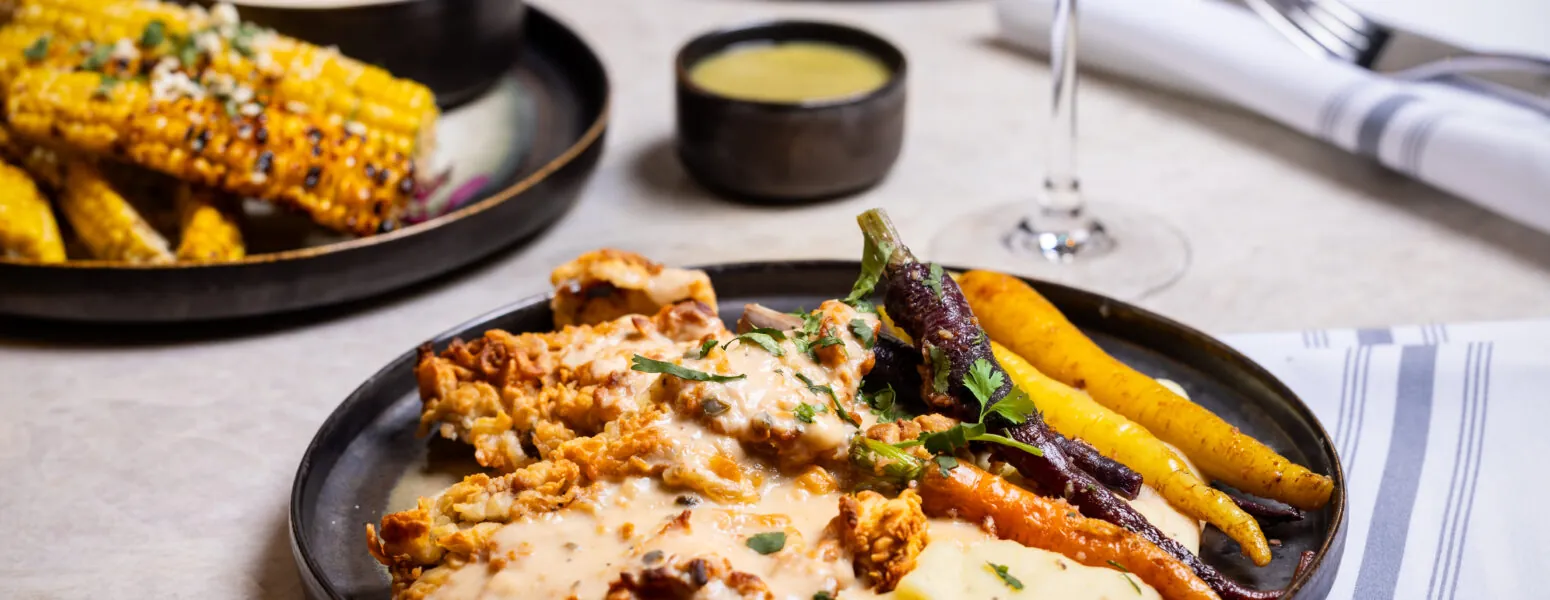 Chicken with patatoes, carrots and sauce on a black plate.