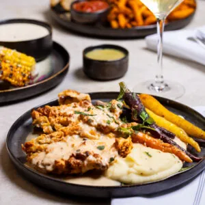 Chicken with patatoes, carrots and sauce on a black plate.
