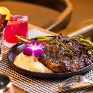Steak with veggies and purple flower garnish.