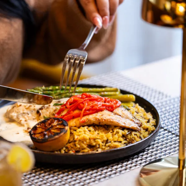 Person eating chicken with rice and flatbread on a black plate.